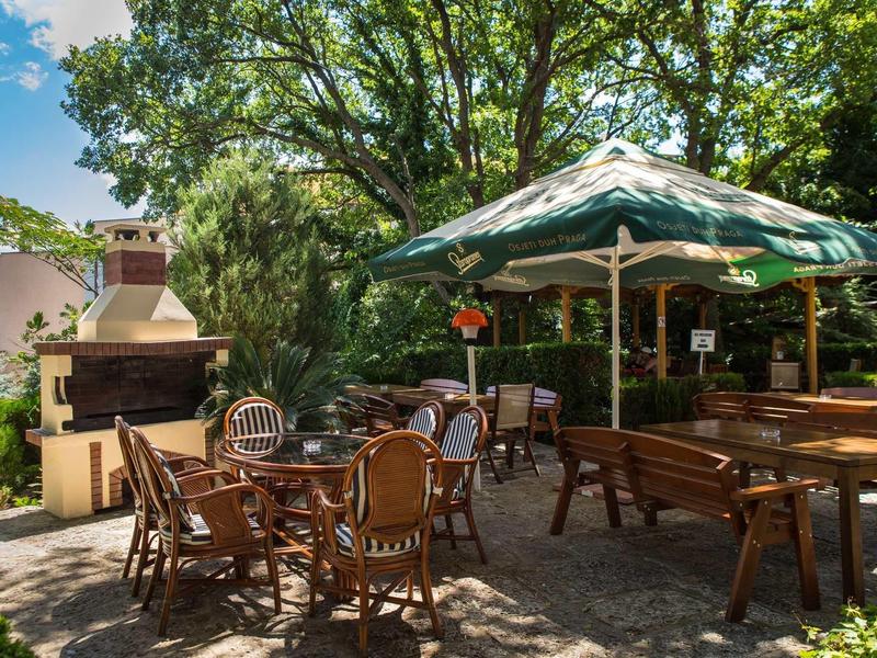 Gemütliche Terrasse mit Holzmöbeln, Sonnenschirm und Kamin, umgeben von grünen Bäumen.