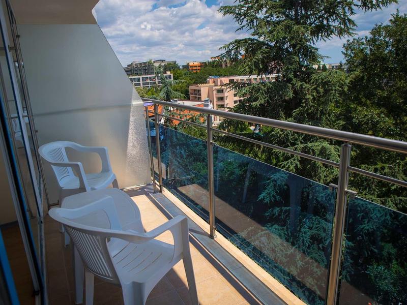 Balkon mit zwei weißen Plastikstühlen, Edelstahlgeländer und Blick auf Bäume und Häuser.