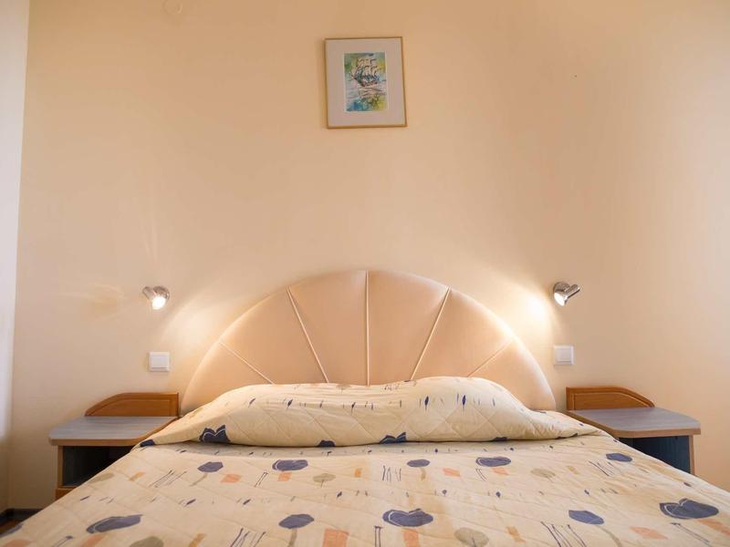 Einfaches Schlafzimmer mit hellen Wänden, Bett mit gebogenem Kopfteil und zwei Nachttischen.