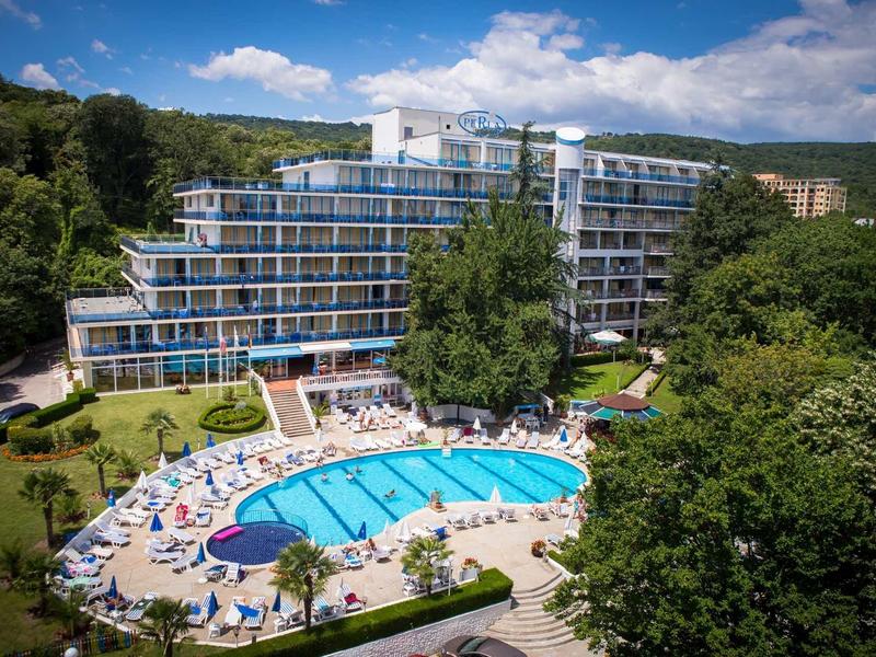 Modernes Hotel mit geschwungenem Pool und Liegestühlen, umgeben von grünen Bäumen und Hügeln.