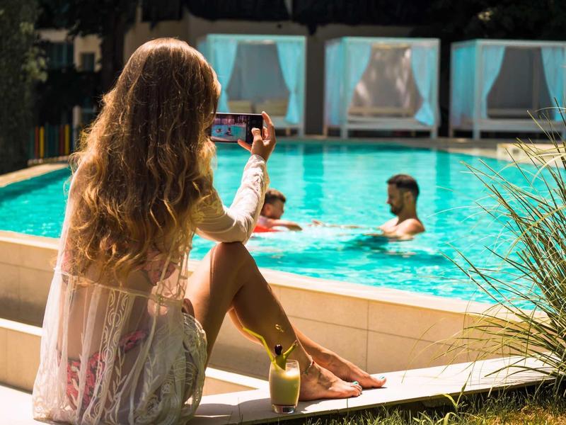 Vrouw zit aan het zwembad en maakt foto van paar dat zwemt.