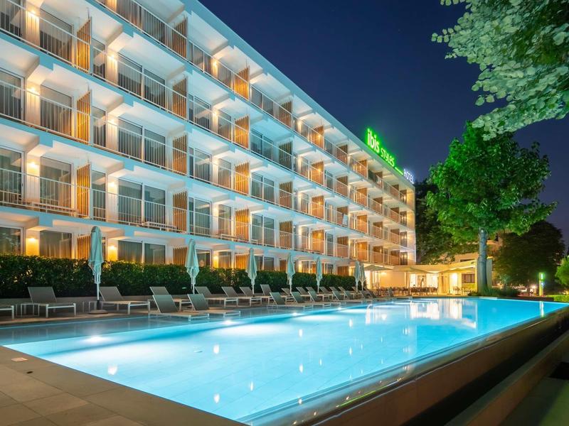 Verlicht zwembad voor een meerlaagse hotelgebouw 's nachts met ligstoelen.