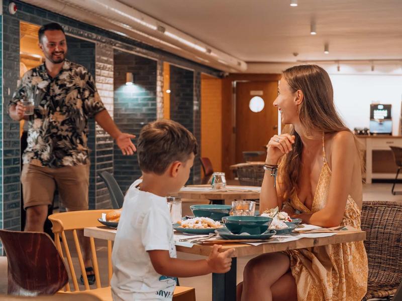 Familie in een gezellig restaurant met eten op tafel en een vriendelijke sfeer.