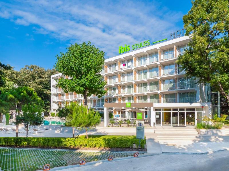 Modern hotelcomplex met balkonkamers, omgeven door bomen en zwembad op de voorgrond.