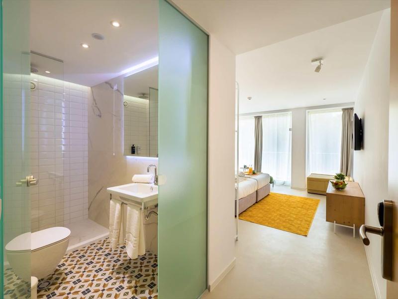 Moderne hotelkamer met badkamer, douche, toilet, eenpersoonsbed en groot raam met gordijnen.