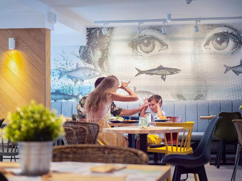 Moeder en kind eten aan een houten tafel in een modern restaurant met muurschildering.