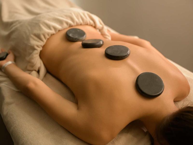 Person's back with hot stones during a wellness massage at the spa.