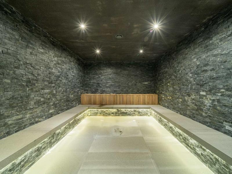 Empty wellness pool with stone walls and wooden benches in a dark room