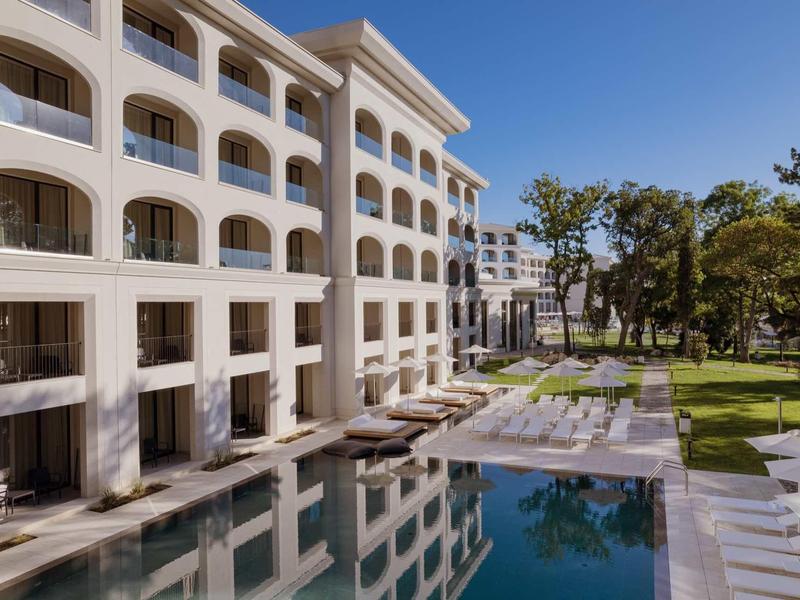 Modern hotel pool with lounge chairs and trees beside a multi-story building.