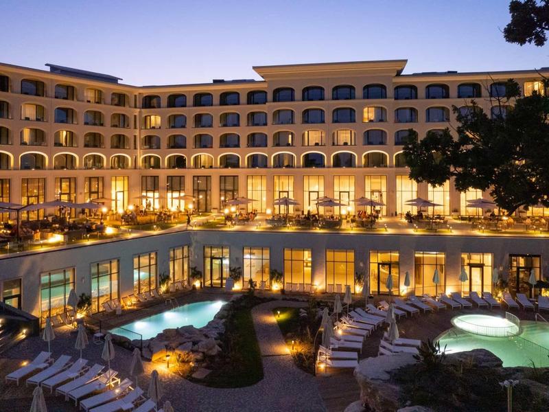 Elegant hotel with illuminated pools and seating areas at dusk.