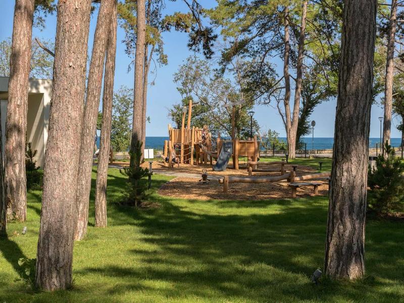 Playground with climbing frame and slide in a park near the lake, surrounded by trees.
