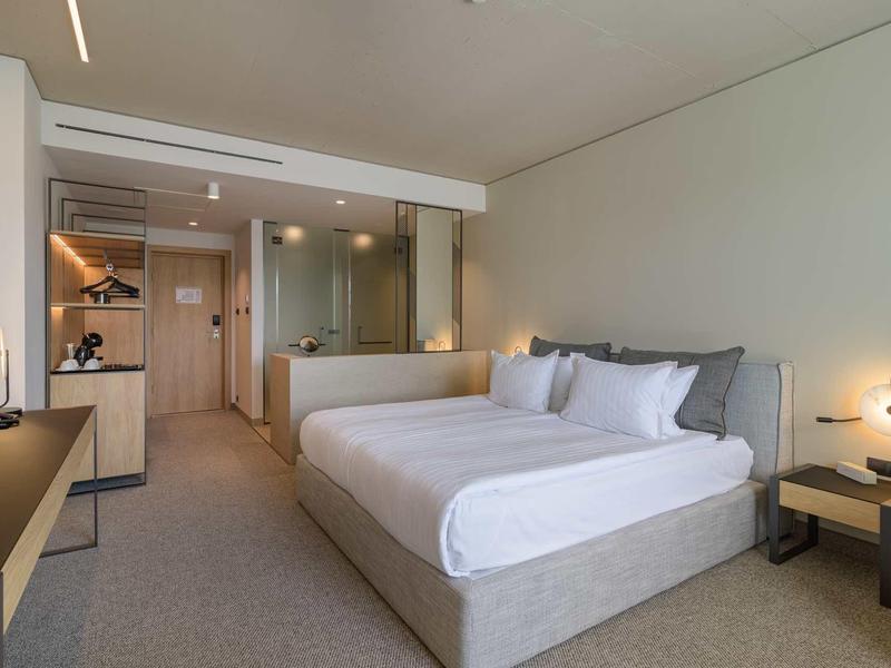 Modern hotel room with large bed, desk, and open bathroom area.