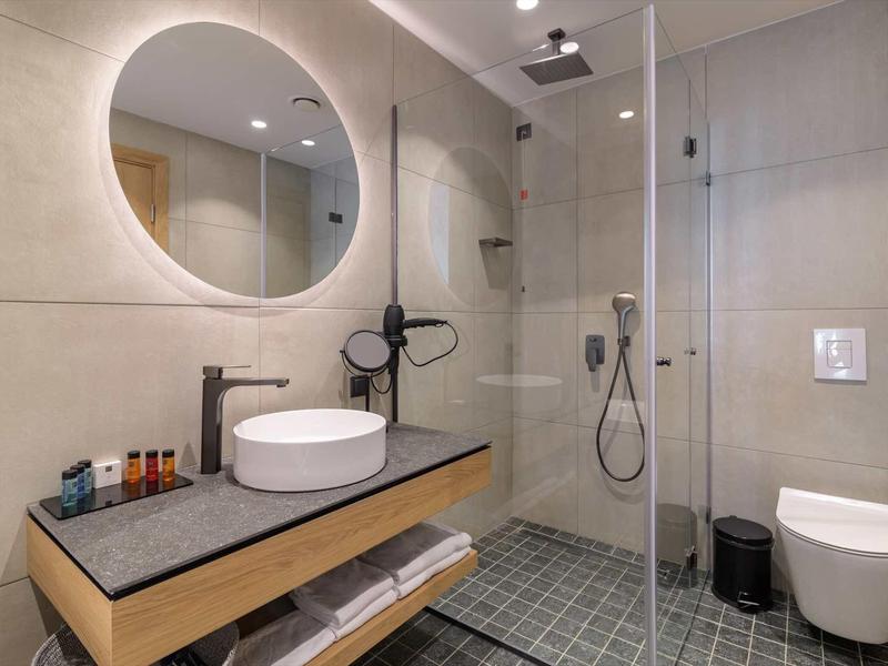 Modern bathroom with round illuminated mirror, sink, and walk-in shower.