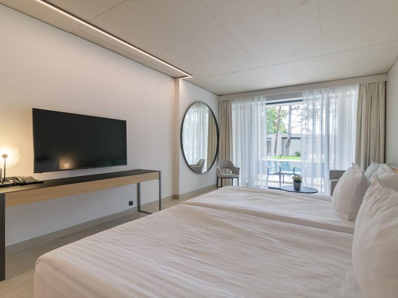 Modern hotel room with large bed, desk, and large window with curtains.