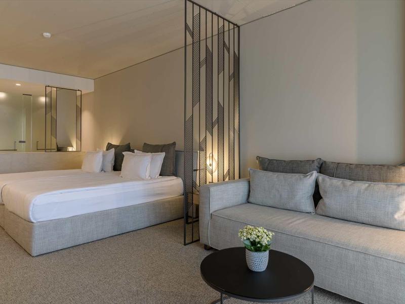 Modern hotel room with double bed, sofa, and table with a small plant.