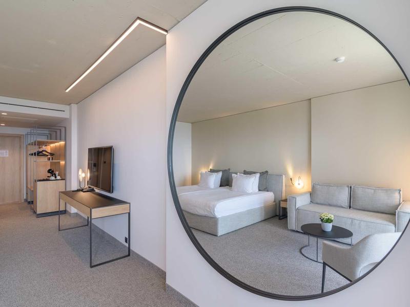 Modern hotel room with large round mirror, double bed, and sofa.