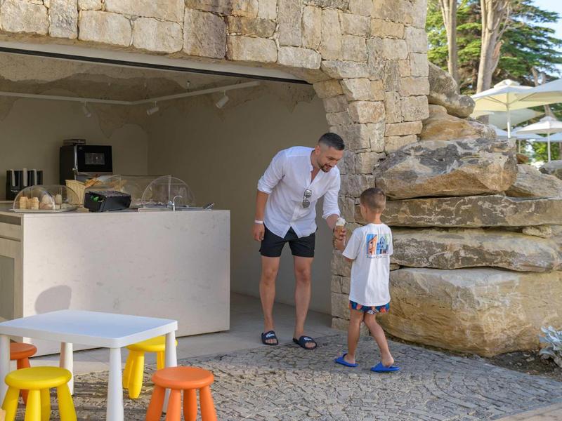 A man and a child stand by an outdoor bar near rocks in a holiday resort.
