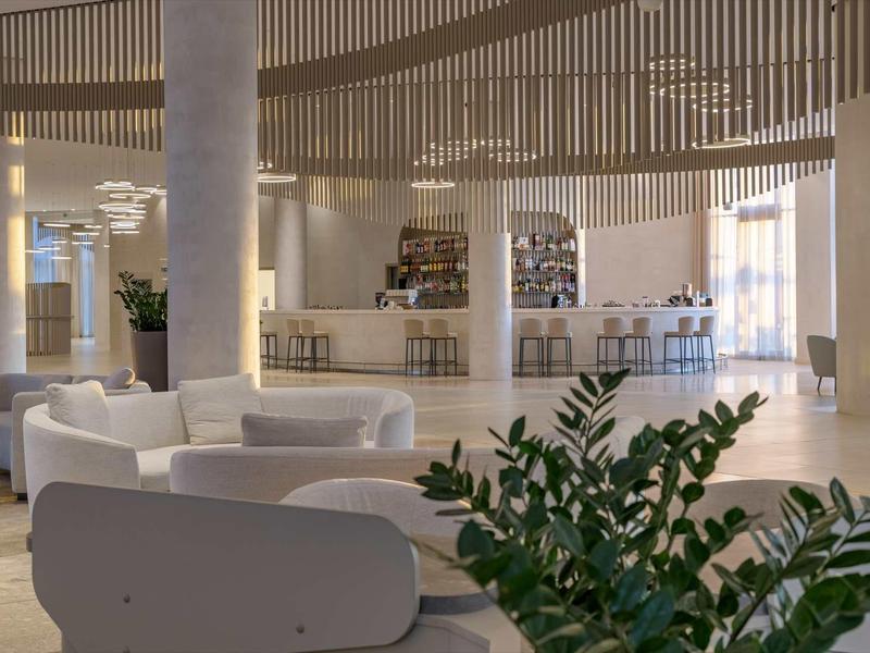 Elegant hotel bar with modern interior, white armchairs, and plants in a bright space.