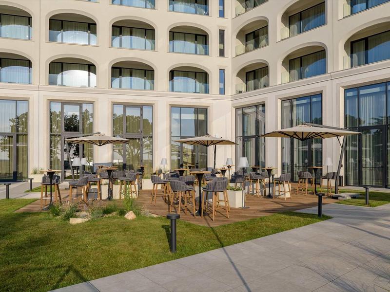 Terrace with tables, chairs, and umbrellas in front of a modern hotel building in daylight