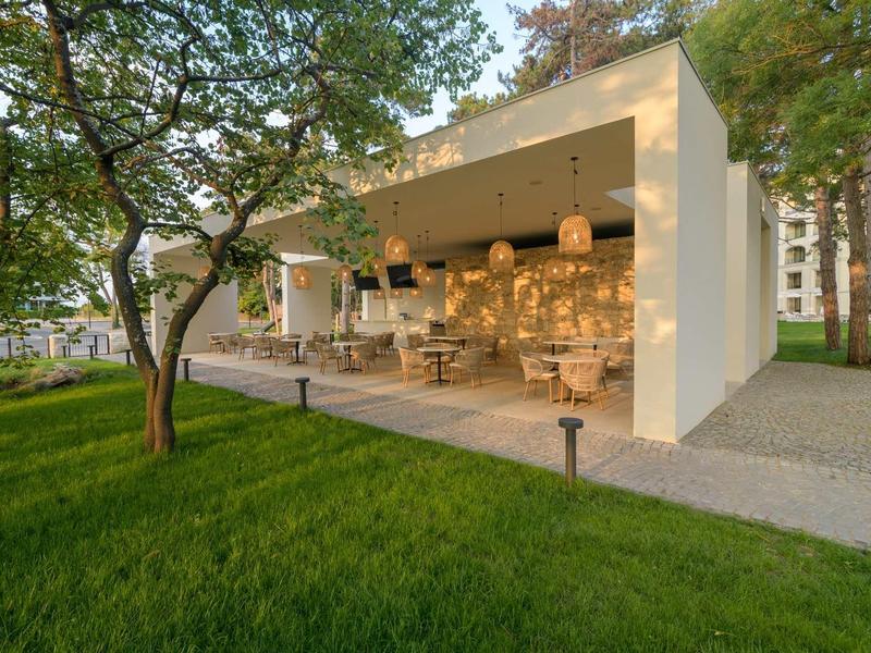 Modern open pavilion with seating areas in a green garden at sunset.