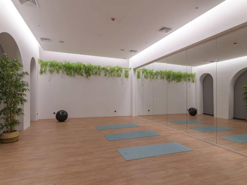 Bright yoga room with wooden floor, mirrored wall, plants, and yoga mats.
