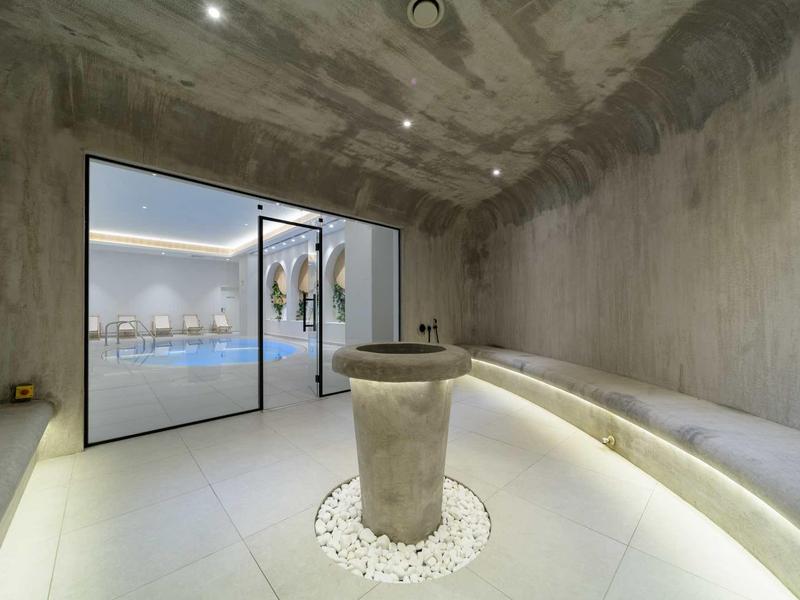 Modern wellness room with concrete walls, central fountain, and view of the pool area.