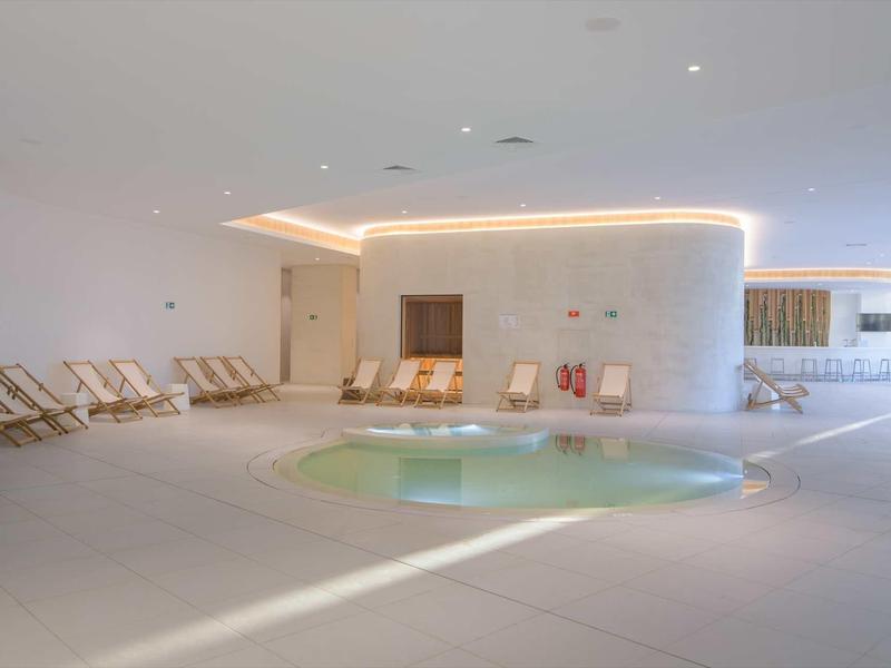 Modern indoor pool area with comfortable lounge chairs and indirect lighting.