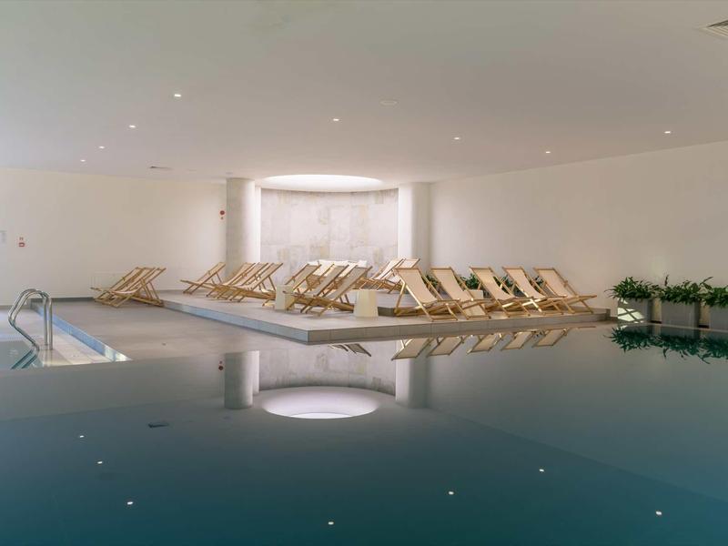 Indoor pool area with lounge chairs and soft lighting in a hotel.