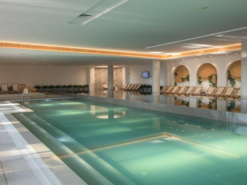 Modern indoor pool with calm water and loungers in a stylish setting.