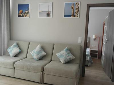 Wohnzimmer mit grauem Sofa und drei Kissen, drei Bilder an der Wand, Blick in angrenzendes Schlafzimmer.