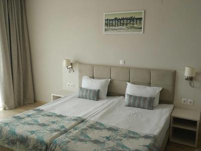 Helles Schlafzimmer mit Doppelbett, grauem Kopfteil, weißen Wänden und zwei Nachttischen.