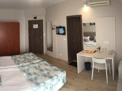 Hotelzimmer mit zwei Betten, Schreibtisch, Stuhl, Schrank, Klimaanlage und TV an der Wand.