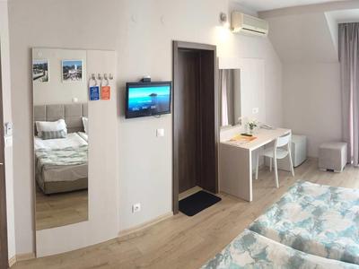 Helles Hotelzimmer mit Doppelbett, Schreibtisch, Wandspiegel und Fernseher, helle Holzböden.