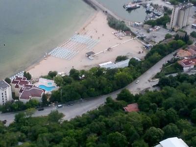 Strand mit Liegen, angrenzende Gebäude und bewaldete Straße im Küstenbereich.