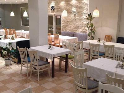 Café mit weißen Tischen, Holzstühlen und warmem Licht, helle Wände und dekorative Pflanzen.