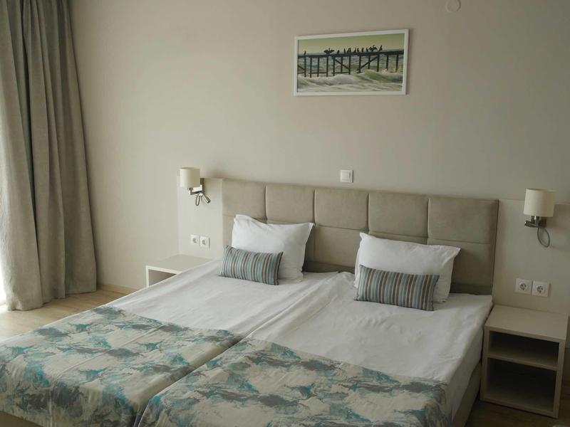 Helles Schlafzimmer mit Doppelbett, grauem Kopfteil, weißen Wänden und zwei Nachttischen.