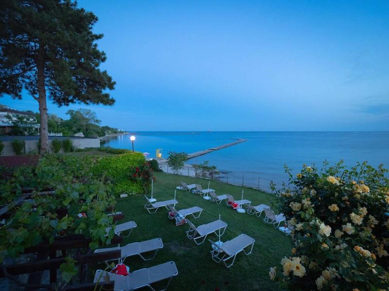 Strand mit Liegestühlen, grünem Rasen, Blumen und ruhigem Meer bei Abenddämmerung.