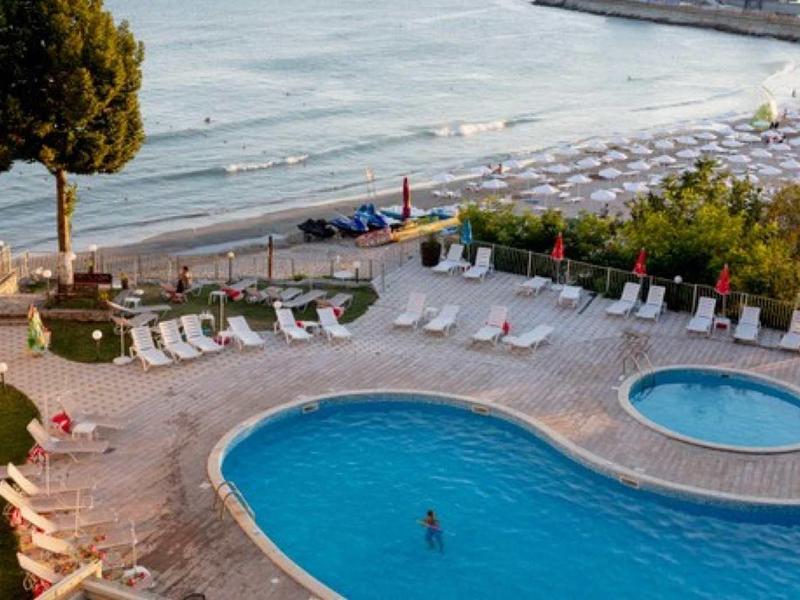 Hotelpool mit Liegestühlen, Sonnenschirmen und Blick auf den Sandstrand und das Meer.