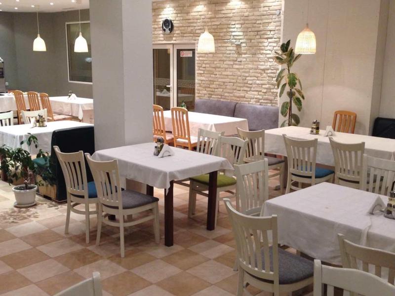 Café mit weißen Tischen, Holzstühlen und warmem Licht, helle Wände und dekorative Pflanzen.