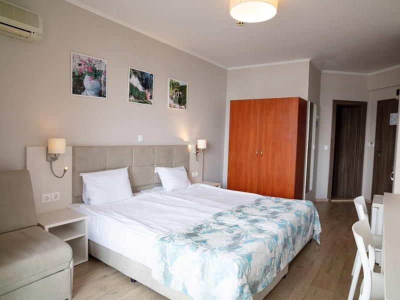 Helles Schlafzimmer mit Doppelbett, weißem Mobiliar, Holzschrank und drei Bildern an der Wand.