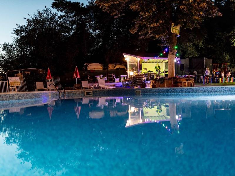 Beleuchteter Pool bei Nacht mit Sitzbereichen und Bäumen im Hintergrund.