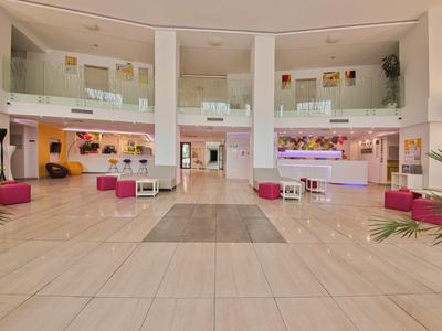 Ruime moderne hotel lobby met witte receptiebalie, zitkussens en lichte marmeren vloer.