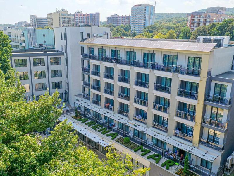 Modern meerlaags hotelcomplex omgeven door bomen en heuvels bij helder weer.