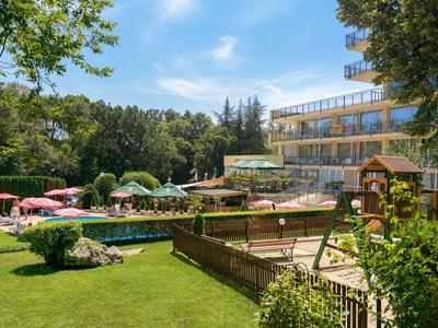 Hotel mit Pool, Sonnenliegen und Kinderspielplatz in einer grünen, sonnigen Umgebung.