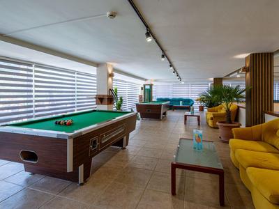 Espace intérieur avec tables de billard, fauteuils jaunes et grandes fenêtres avec stores.