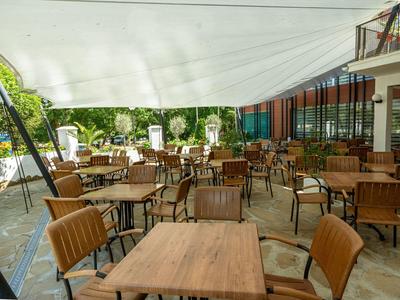 Überdachter Außenbereich eines Restaurants mit Holzstühlen und Holztischen unter einem weißen Sonnensegel.