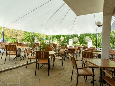 Große, überdachte Außenterrasse mit Holztischen und -stühlen in einem grünen Garten