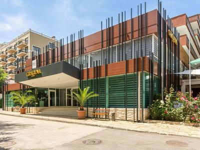 Modernes Hotel mit großem Vordach, vertikalen Säulen und Palmen im Eingangsbereich.