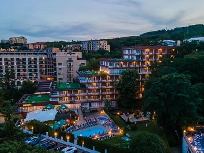 Beleuchtetes Hotel mit Pool und umliegender grüner Landschaft bei Abenddämmerung.