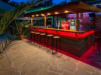 Beleuchtete Außenbar mit Hockern unter einem Holzdach bei Nacht.